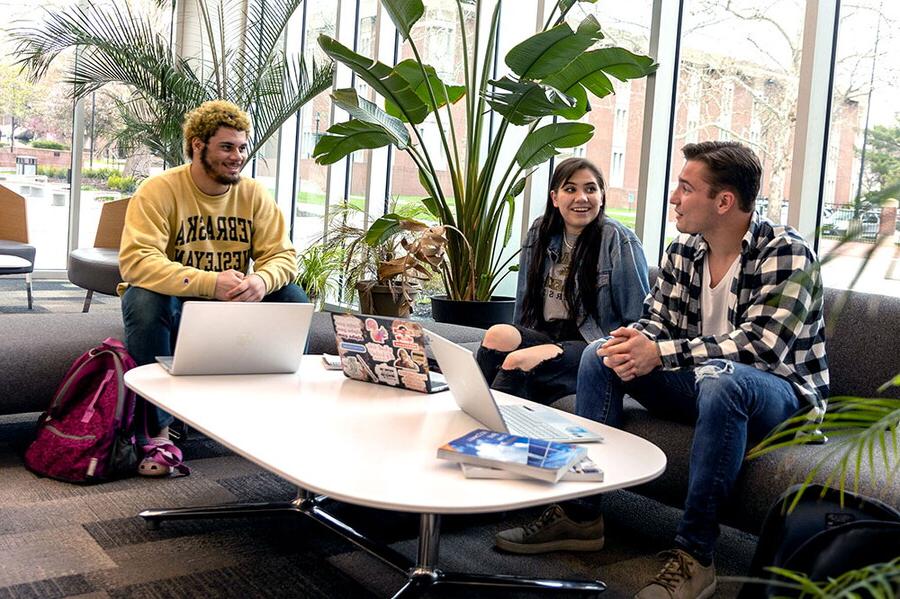 Three students study in the lobby of the Acklie building at a table.